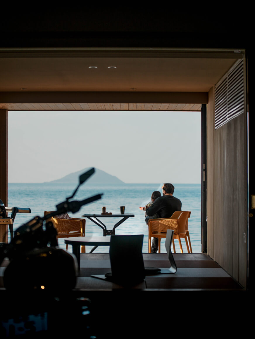 室内に駐輪したバイク越しに海を眺める